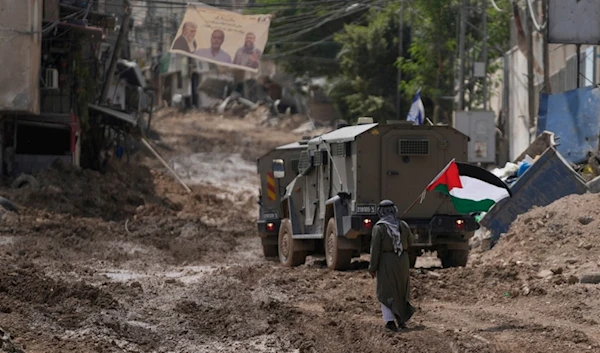 A man waves a Palestinian flag as he walks past an Israeli occupation armored vehicle during a military operation in the West Bank refugee camp of Tulkarem, West Bank, Palestine, Sept. 4, 2024. (AP)