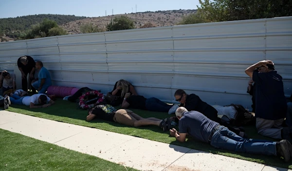 People take cover as a siren warns of incoming rockets fired from Lebanon, at the Tel Regev cemetery in the outskirts of Haifa, northern occupied Palestine, Monday, Oct. 21, 2024. (AP)