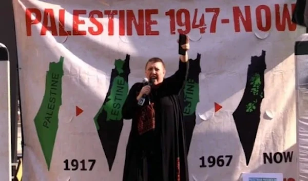 Charlotte Lynne Kates, director of the Samidoun Palestinian Prisoner Solidarity Network, in an undated photo, stands before a banner displaying the annexation of Palestine (Social Media)