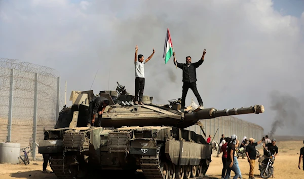 Gazans celebrate by a destroyed Israeli tank at the broken border fence, east of Khan Younis, October 7, 2023. (AP)