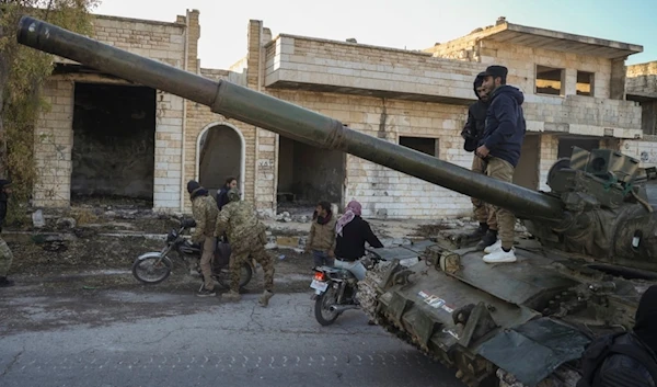 Syrian terrorists get on a motorcycle as opposition supporters stand on top of a captured army armored vehicle in the town of Maarat al-Numan, southwest of Aleppo, Syria, Saturday, November 30, 2024 (AP)