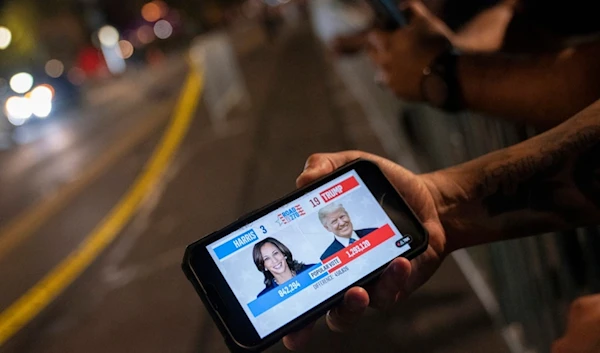 A member of the Metropolitan Police Department watches live election coverage outside of election night event for Democratic presidential nominee Vice President Kamala Harris at Howard University in Washington, Tuesday, November 5, 2023 (AP)