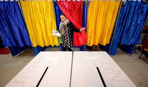 A woman exits a voting cabin with the colors of the Romanian flag as curtains before casting her vote in the country's parliamentary elections, in Bucharest, Romania, Sunday, December 1, 2024 (AP)