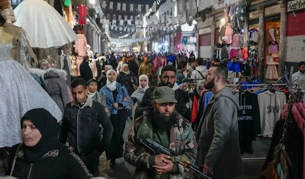 An armed opposition fighter walks among costumers at the al-Hamidiyeh market inside the old walled city of Damascus, Syria, Tuesday, December 10, 2024 (AP)