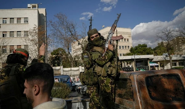 A masked fighter holds his gun as people walks by on their way to a celebratory demonstration in Damascus' central square, Syria, Friday, Dec. 13, 2024. (AP)