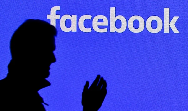 A man passes a facebook screen at the Gamescom in Cologne, Germany, Tuesday, Aug. 20, 2019. (AP)