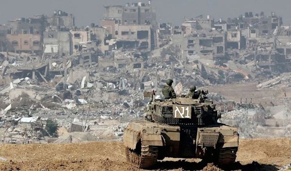 Israeli soldiers stationed atop a tank overlook residential areas in northern Gaza destroyed by Israeli bombardment in January 2024 (AFP)