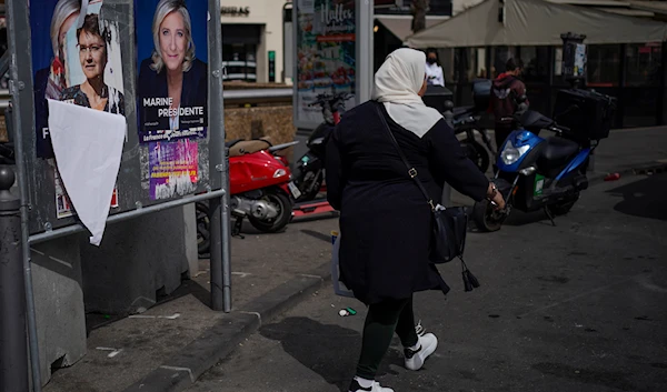 A woman walks by presidential campaign posters in Marseille, southern France, on April 13, 2022 (AP)