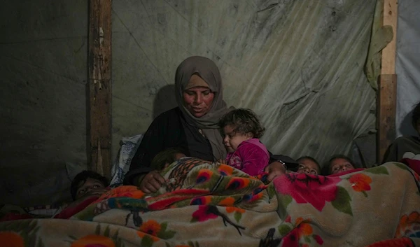 Reda Abu Zarada wraps herself and her grandchildren in blankets as they prepare to sleep in their tent at a camp in Khan Younis, Gaza Strip, on December 19, 2024. (AP)