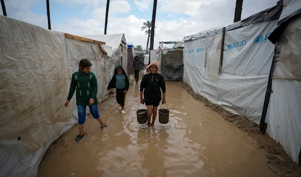 Palestinian children carry buckets of water after overnight rainfall at the refugee tent camp for displaced Palestinians in Deir al-Balah, central Gaza Strip, Tuesday, Dec. 31, 2024. (AP)