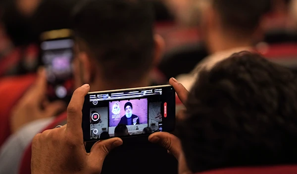 A man films a speech by Hezbollah leader Sayyed Hassan Nasrallah with a mobile phone as speaking via a video link, in the southern suburbs of Beirut, Lebanon, May 14, 2024 (AP)