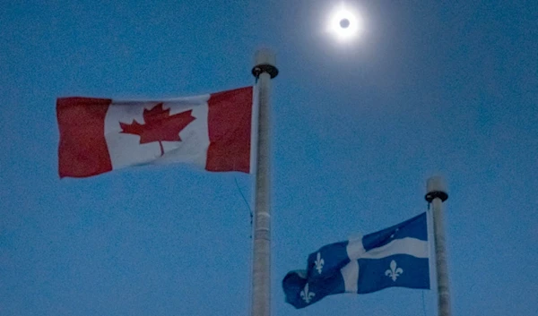 The moon covers the sun during a total solar eclipse, as Canadian and Quebec flags fly, as seen from Bishop's University in Sherbrooke, Quebec, Monday, April 8, 2024. (AP)