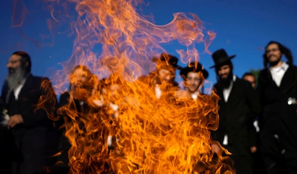 Ultra-Orthodox Jews dance around a bonfire during Lag B'Omer celebrations at the traditional grave site of Rabbi Shimon Bar Yochai at Jabal al-Jarmaq, occupied Palestine, Thursday, May 19, 2022 (AP)