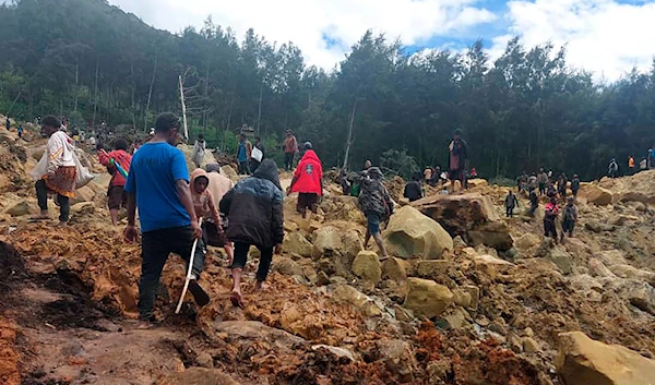 In this photo provided by the International Organization for Migration, people cross over the landslide area to get to the other side in Yambali village, Papua New Guinea, Friday, May 24, 2024. (AP)