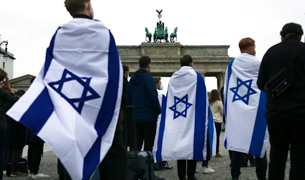 People, some draped with Israeli occupation flags attend a rally in solidarity with Israel near the Brandenburg Gate in Berlin, Germany, Wednesday, May 12, 2021. (AP)