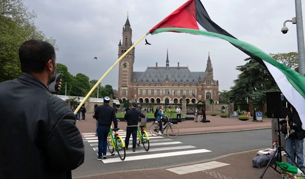 A lone demonstrator waves the Palestinian flag outside the Peace Palace, rear, housing the International Court of Justice, or World Court, in The Hague, Netherlands, Friday, May 24, 2024.