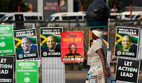 A woman walks past election posters in Tembisa, east of Johannesburg, South Africa, Tuesday, May 28, 2024, ahead of the elections on Wednesday May 29. (AP)