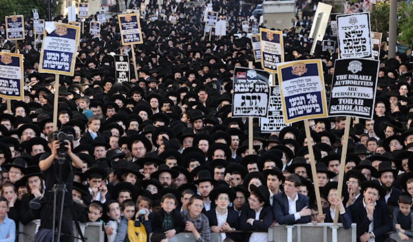 Ultra-Orthodox Jewish men and youth raise placards during a protest against Israeli army conscription outside an army recruitment office in al-Quds on April 11, 2024. (AFP)