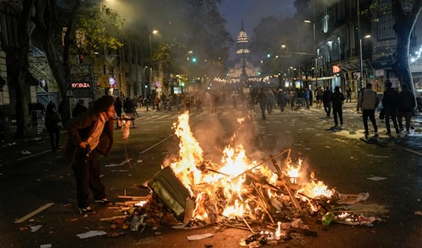 A man lights a cigarette from trash set alight by anti-government protesters outside Congress, where lawmakers debate a reform bill promoted by Argentine President Javier Milei in Buenos Aires, Argentina, Wednesday, June 12, 2024. (AP)