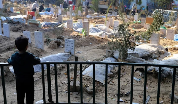 A Palestinian child looks at the graves of people killed in the Israeli bombardment of the Gaza Strip and buried inside the Shifa Hospital grounds in Gaza City, Sunday, Dec. 31, 2023. (AP)