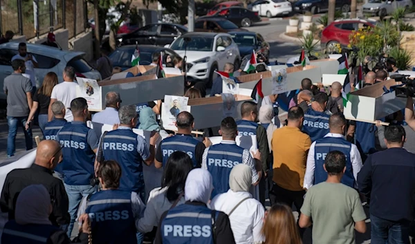 Palestinian journalists carry mock coffins of Palestinian journalists who were killed during the current war in Gaza during a symbolic funeral toward a United Nations office, in the West Bank city of Ramallah, Tuesday, Nov. 7, 2023 (AP)