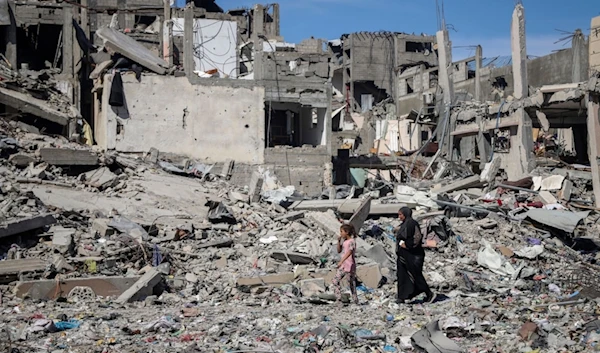 A Palestinian woman and girl walk through rubbles of destroyed homes in northern Gaza, Friday, May 31, 2024. (AP Photo/Enas Rami)