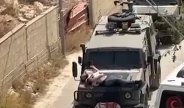 An injured Palestinian civilian tied by Israeli forces to the front of a military Jeep in Jenin (Screen Grab)