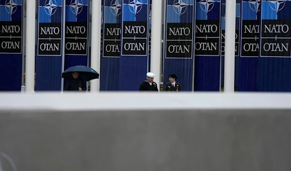 Two military personnel walk by NATO banners prior to a wreath laying ceremony at NATO headquarters in Brussels, Thursday, April 4, 2024. (AP)