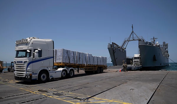 US Army soldiers stand next to trucks arriving loaded with humanitarian aid at the US-built floating pier Trident before reaching the beach on the coast of the Gaza Strip, occupied Palestine, June 25, 2024 (AP)