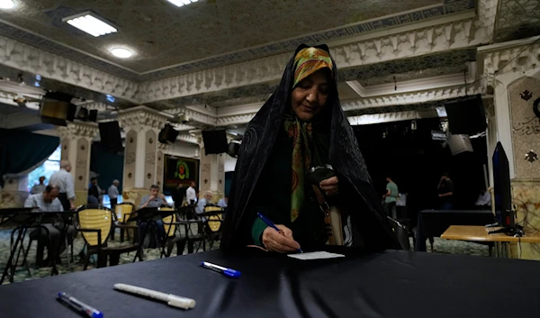 An elderly woman uses a magnifying glass to fill out her ballot for the presidential election at a polling station in Tehran, Iran, June 28, 2024 (AP)