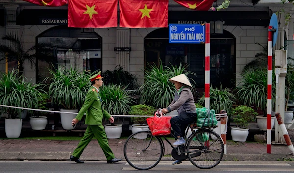 A woman rides a bicycle as a policeman walks past Vietnam flags in Hanoi, Vietnam, on February 27, 2019. (AP)