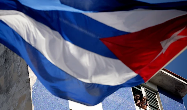 couple look out from a balcony past Cuba's national flag at a march marking the 140th anniversary of the execution of eight Cuban medical students by the Spanish colonial government during Cuba's Ten Years' War, in Havana, Cuba, on November 27, 2011. (AP)