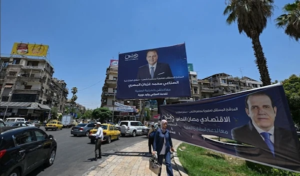 People walk past electoral campaign posters ahead of parliament elections in Damascus, Syria, on July 10, 2024. (AFP)