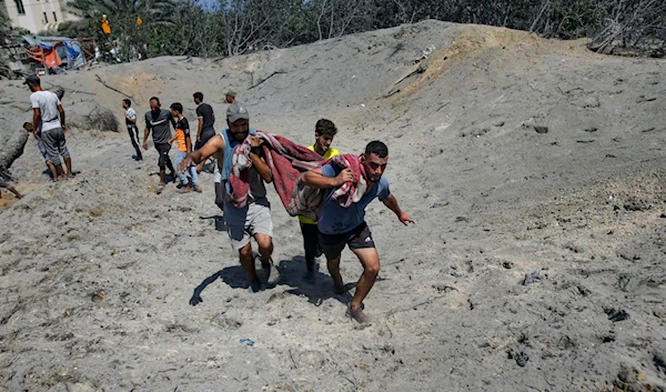 Palestinians evacuate a person killed by the Israeli occupation forces from a site hit by an Israeli bombardment on Khan Younis, southern Gaza Strip, July 13, 2024 (AP)