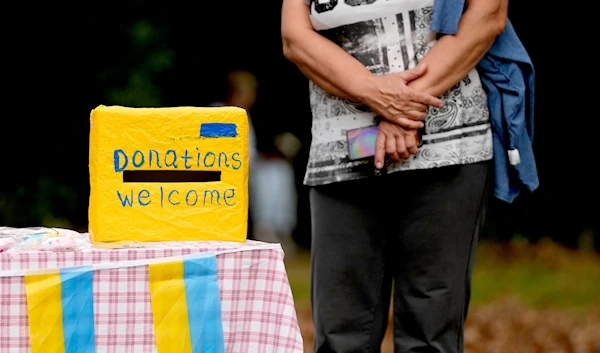 A woman waits near a donation box at the celebration for the Ukraine Independence day at a celebration in Chichester, south England, Saturday, Aug. 27, 2022.(AP)