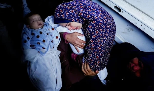 A Palestinian mother Rania Abu Anza's holds one of her five-month-old twins who were killed alongside her husband, and 11 other relatives in an Israeli airstrike. (@hamdahsalhut)