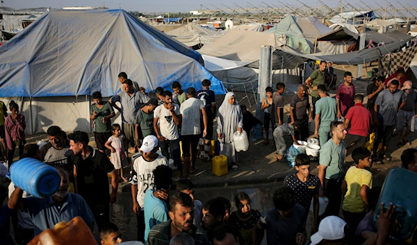 Palestinians displaced by the Israeli bombardment of the Gaza Strip queue for water at a makeshift tent camp in the southern town of Khan Younis, Monday, July 1, 2024. (AP)