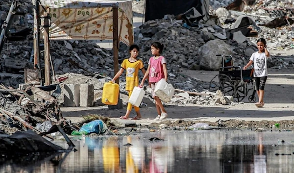 Palestinian girls walk past a lake of sewage leaking from targeted underground pipes by Israeli bombardment in Gaza's second city of Khan Younis amid the ongoing genocide (AFP)