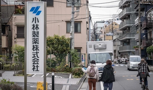 A woman points her finger at the signage of Kobayashi Pharmaceutical as she walks past the company's office in Tokyo on March 28, 2024. (AFP)