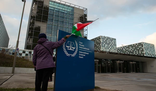 A demonstrator poses with a Palestinian flag outside the International Criminal Court during a rally urging the court to prosecute "Israel" for war crimes, in The Hague, Netherlands, November 29, 2019. (AP)