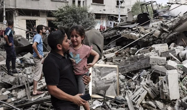 A Palestinian father carries his crying son as he walks in front of a building destroyed in an Israeli air strike in Gaza City on October 7, 2023. (AFP)