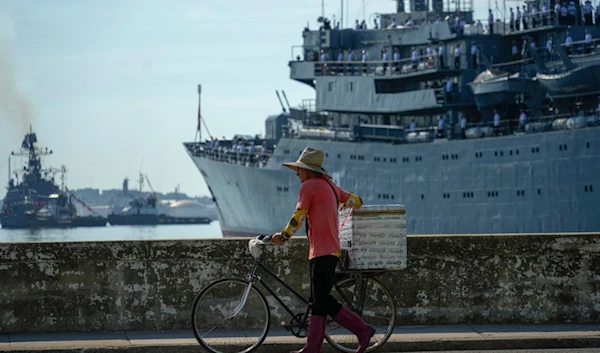 A street vendor walks his bicycle by the Russian training ship Smolnyy as it arrives for a working visit, in the bay of Havana, Cuba, Saturday, July 27, 2024. (AP)