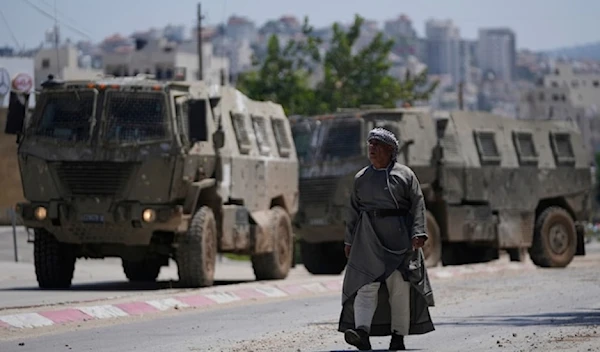 A Palestinian man walks past two Israeli military personal carriers during an Israeli raid on the occupied west bank refugee camp of Tulkarm, on Tuesday, July 23,202. (AP)