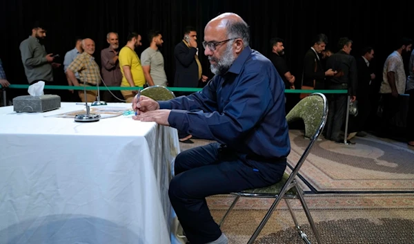 A man fills out his ballot as others line up during the presidential election in a polling station at the shrine of Saint Saleh in northern Tehran, Iran, Friday, July 5, 2024. (AP)