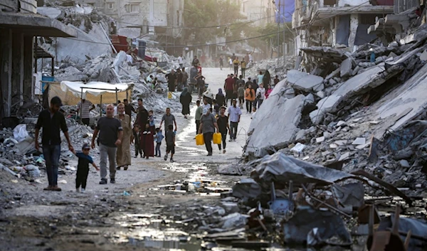 Palestinians displaced by the Israeli air and ground offensive on the Gaza Strip, walk through a dark streak of sewage flowing into the streets of the southern town of Khan Younis, Gaza Strip, Thursday, July 4, 2024. (AP)