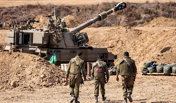 Israeli army soldiers walk near a self-propelled howitzer stationed near the border with Gaza, October 12, 2023. (AFP)