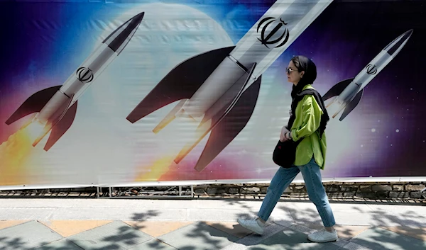 A woman walks past a banner showing missiles being launched, in northern Tehran, Iran, April 19, 2024 (AP)