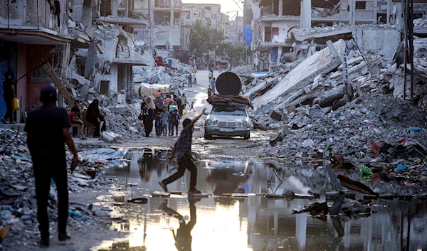 Palestinians displaced by the Israeli air and ground offensive on the Gaza Strip, walk past sewage flowing into the streets of the southern town of Khan Younis, Gaza, July 4, 2024 (AP)