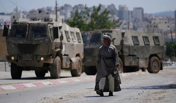 A Palestinian man walks past two army personal carriers during an Israeli army raid in the occupied West Bank refugee camp of Tulkarem, in Tulkarem, July 23, 2024. (AP)