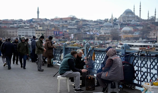 People warm themselves with a fire while fishing over the Galata bridge in Istanbul, Turkey, Wednesday, Feb. 21, 2024. (AP)